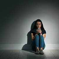 Female young adult sitting alone in an empty room using a cell phone