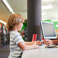 Child in library receiving library card from offscreen adult