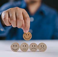 Hand selecting a smiley face tile out of a selection of sad face tiles.