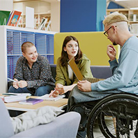 Three young people, one in a wheelchair, having a conversation in a library.