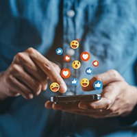 Decorative image of person holding a mobile device with emojis representing social media floating above it.