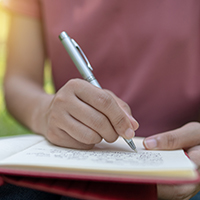 Decorative close up image of a young person holding a pen and writing in a journal.
