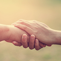 Photo of one person’s hands holding another person’s hand in a comforting manner.