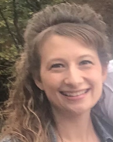 Smiling woman with light brown curly hair wearing a jean jacket. 
