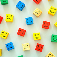 Image of multi-colored wooden blocks with faces showing different emotions drawn on each block face in black ink.
