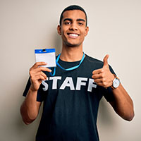 Male person of color wearing a staff tshirt and holding a staff badge.